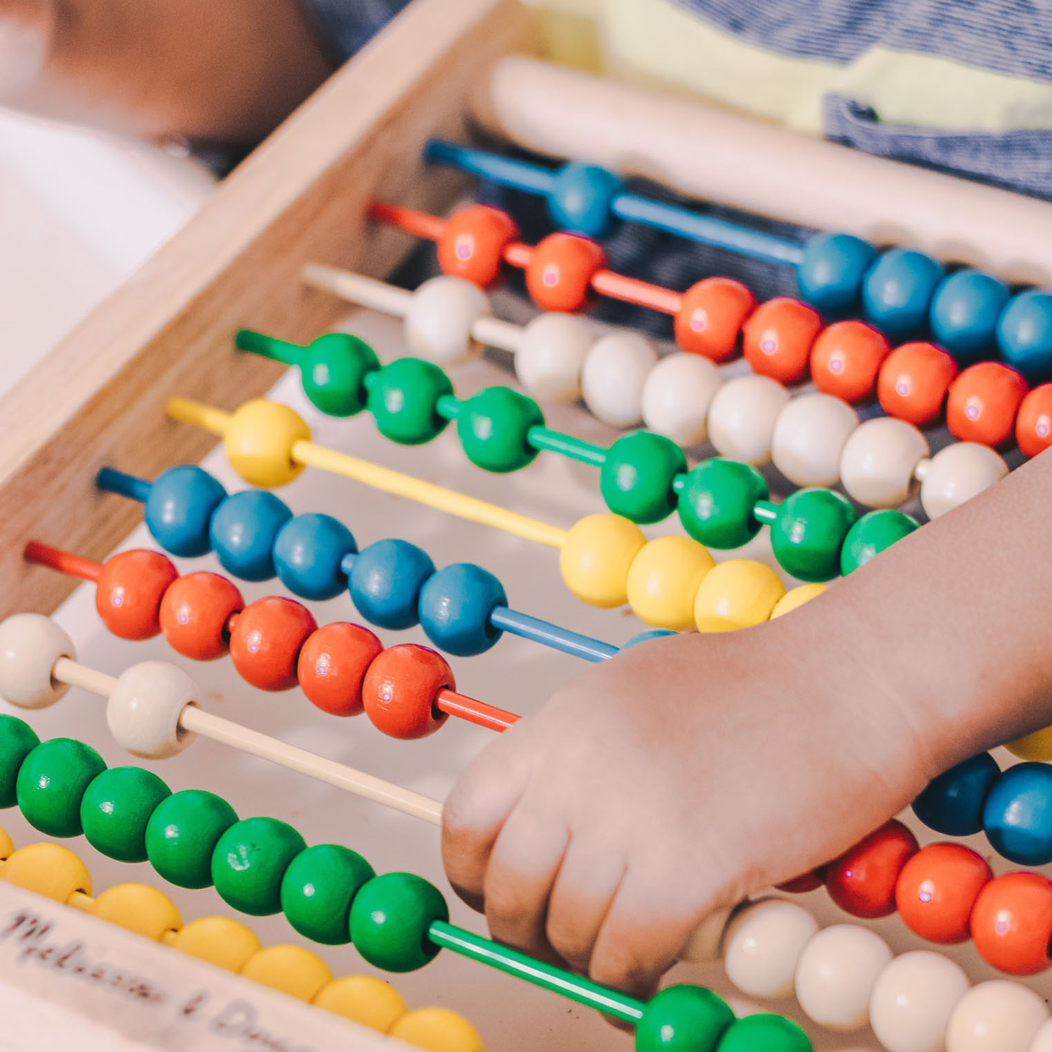 A child has their hand on an abacus. The abacus is blue, red, cream, green and yellow.